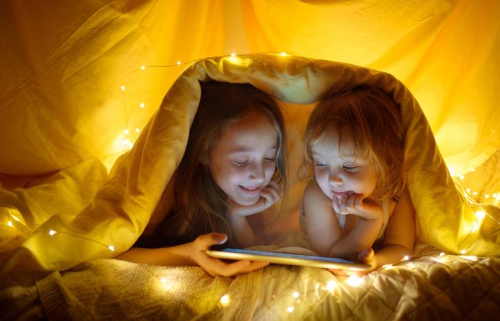 To småjenter leser nettbrett i telt