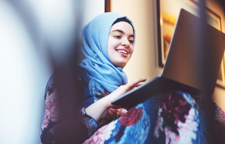 Ung kvinne fra Midtøsten med hijab skriver på pc