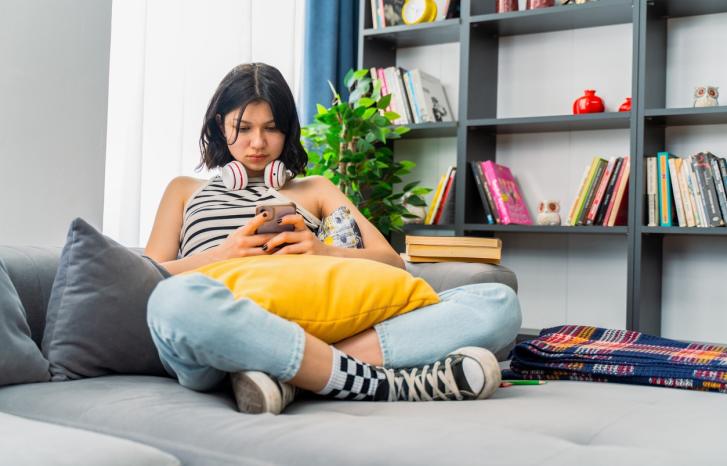 Ung jente sitter på senga med gul pute og mobil i fanget