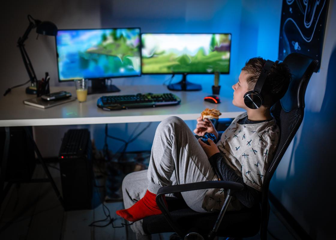 Gutt som sitter foran to dataskjermer med spillgrafikk på