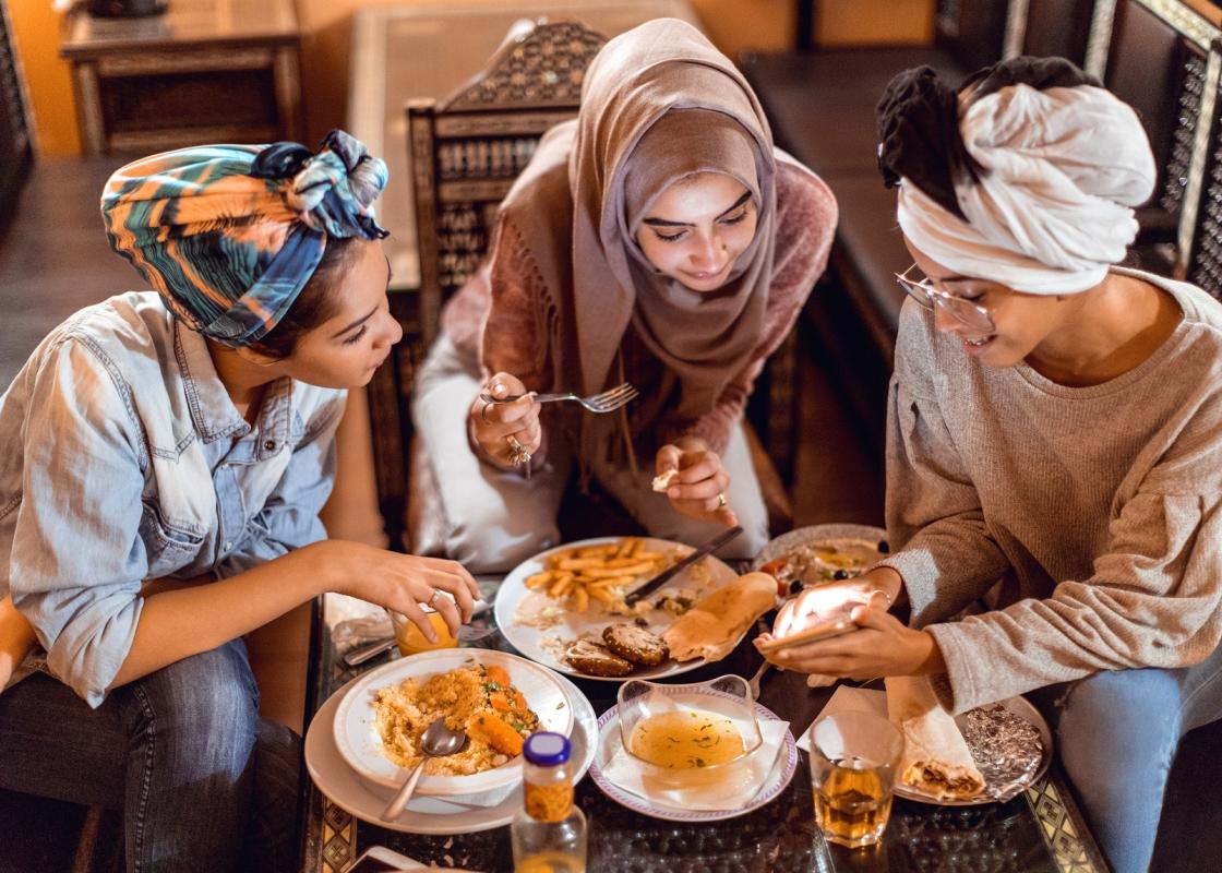 Tre kvinner med ulike typer hodetørkle sitter rundt et bord med mat 