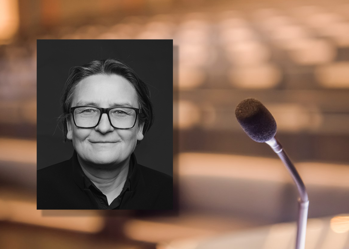 Portrettfoto av Ragnhild Hennum, dekan ved UiO, mot bakgrunn med mikrofon og tomme stolrader