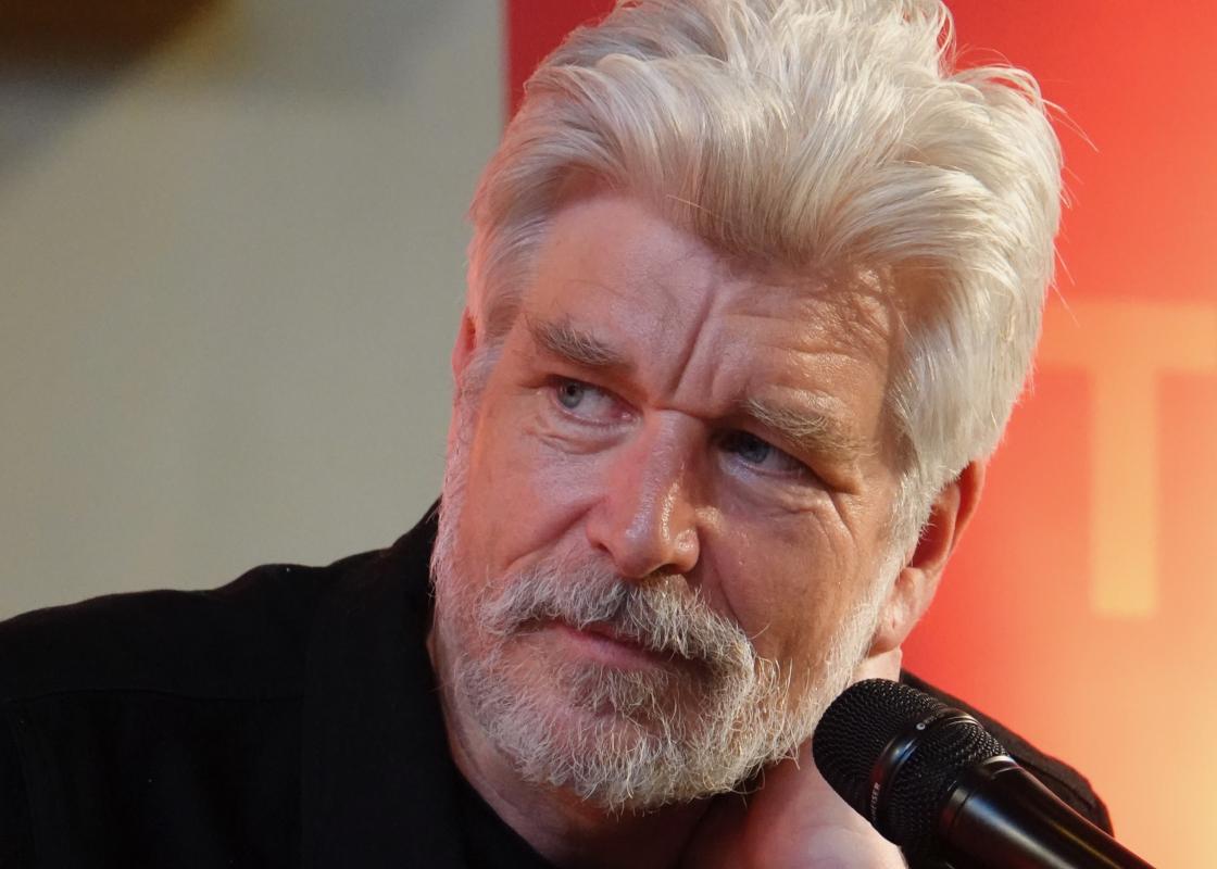 Portrettfoto av forfatter Karl Ove Knausgård med mikrofon mot oransje bakgrunn