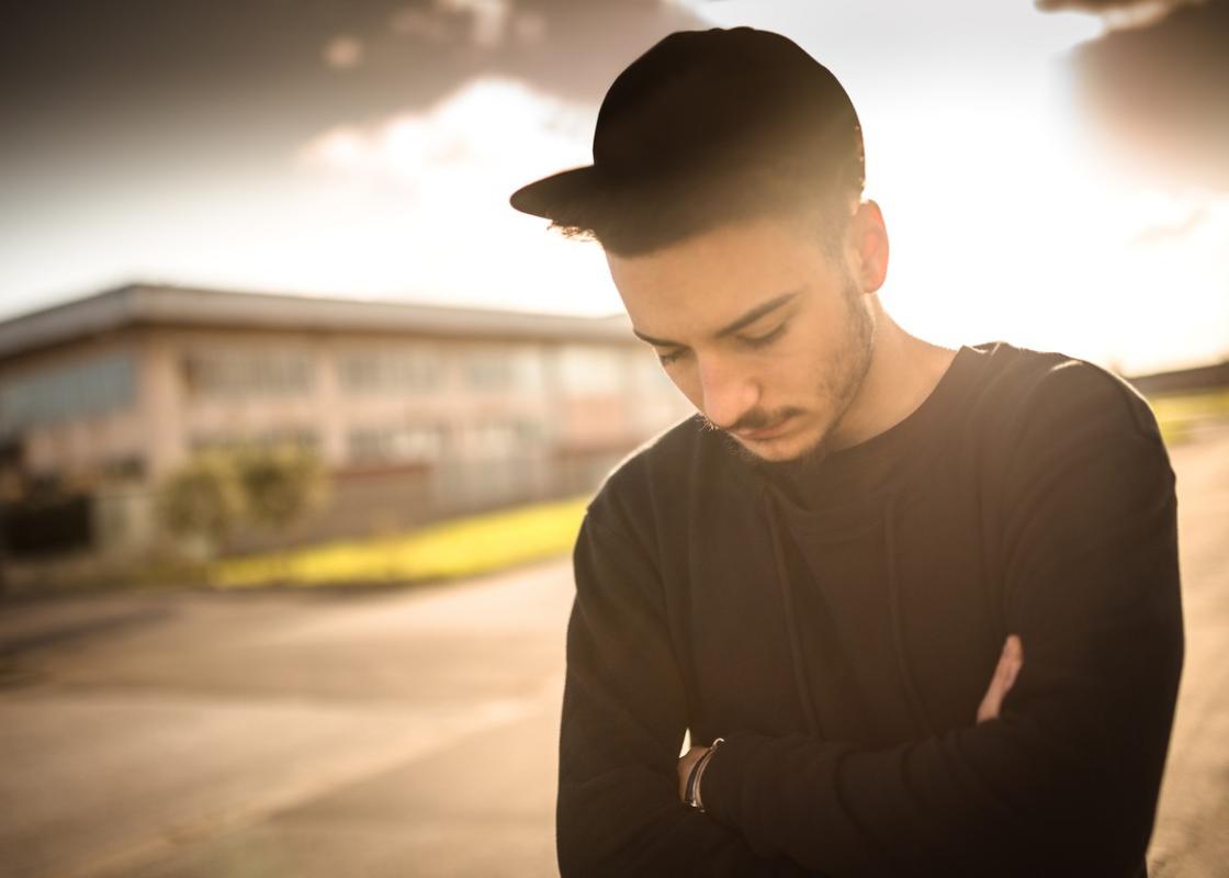 Ung, svartkledd mann med caps ser ned i bakken