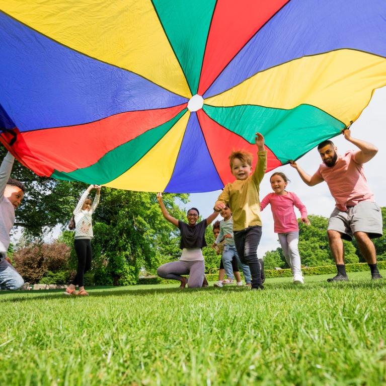 Barn og to voksne leker under et fargerikt segl