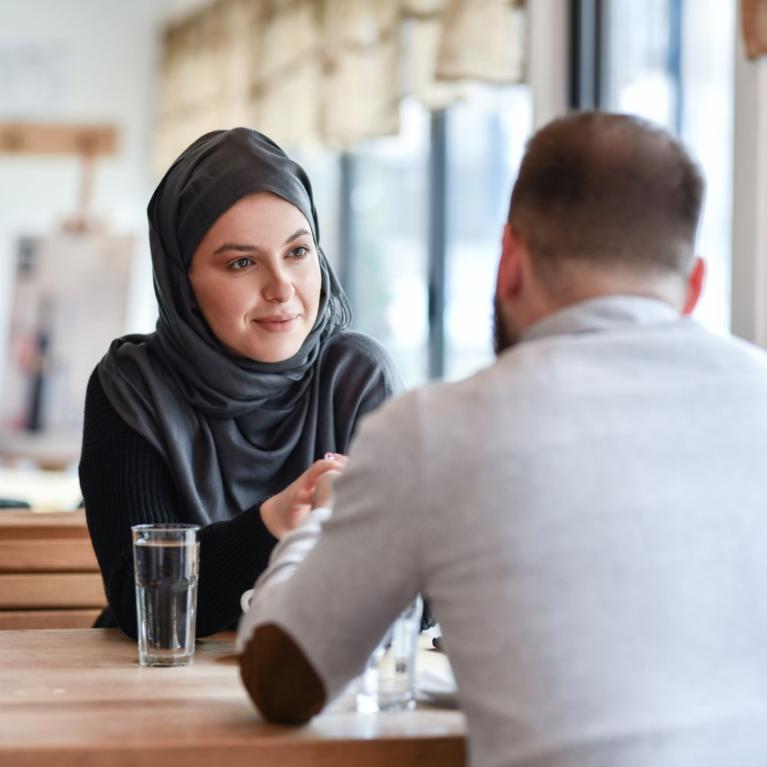 Kvinne med hijab og mann med ryggen til sitter på kafe
