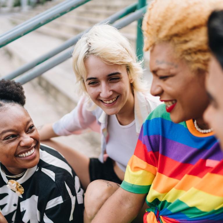 Skeive ungdommer med fargerike klær som prater og smiler, sittende i en trapp