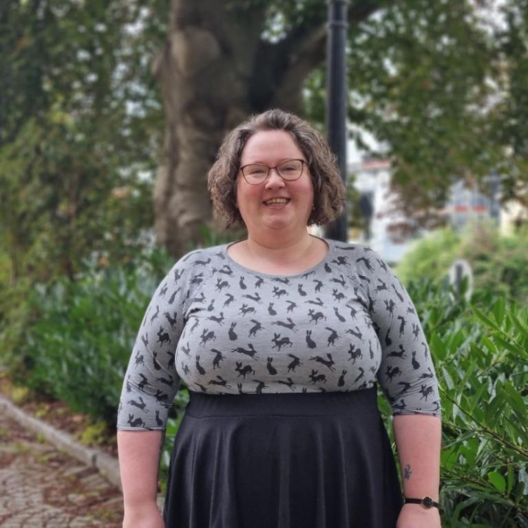 Sunniva Árja Tobiasen, stipendiat ved senter for kvinne- og kjønnsforskning ved Universitetet i Bergen fotografert omgitt av grønne trær