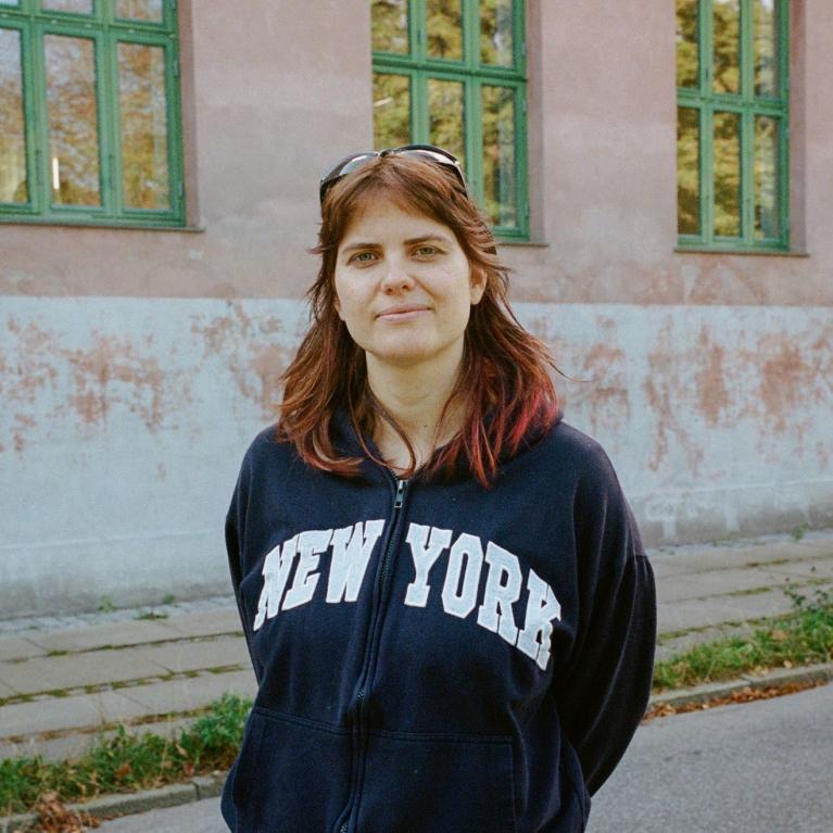 Portrettfoto av Amalie Sehested Rom, stipendiat ved UiO, foran en rosa leiegård med grønne karmer.