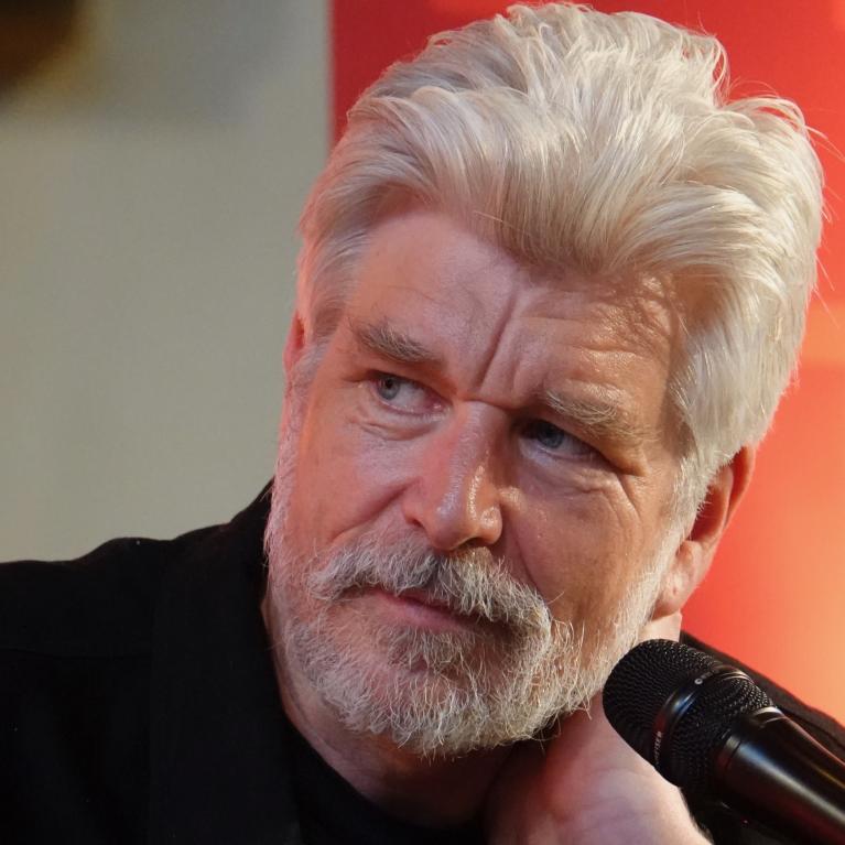 Portrettfoto av forfatter Karl Ove Knausgård med mikrofon mot oransje bakgrunn