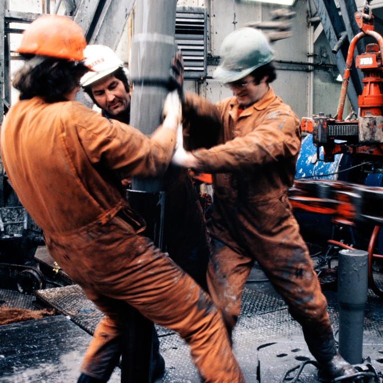 Tre arbeidere i verneutstyr jobber med boring på oljeplattform