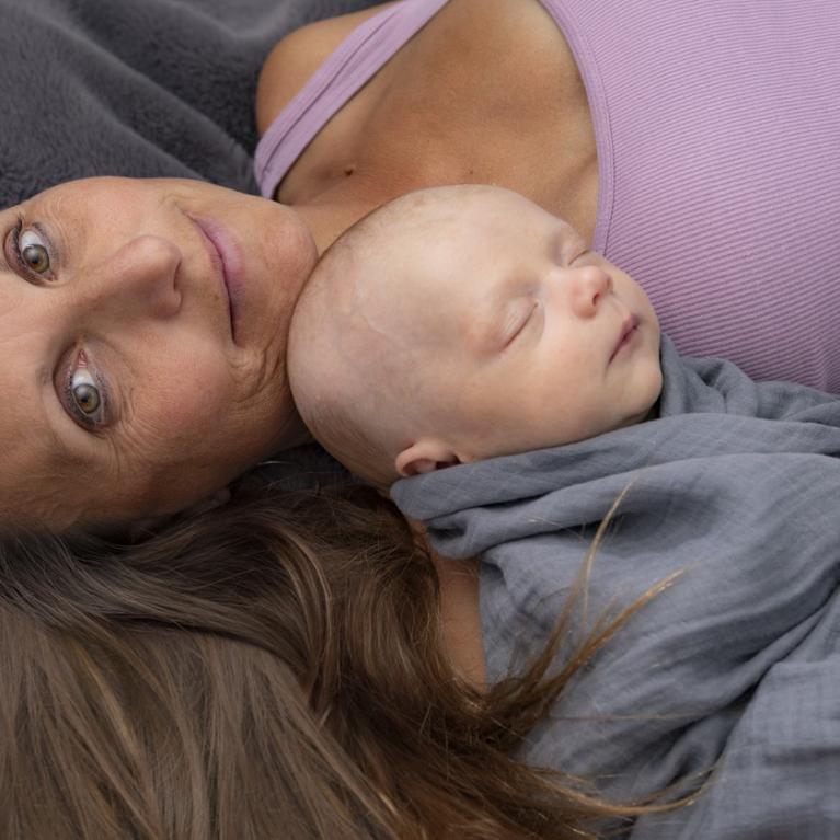 Godt voksen kvinne ligger med sovende baby på brystet