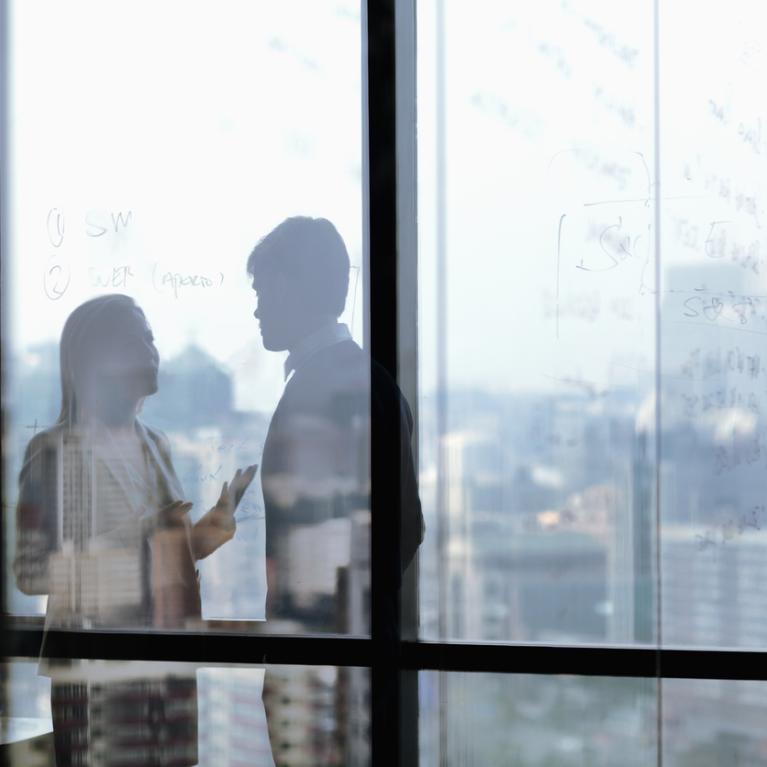 To personer i samtale bak en glassvegg